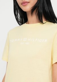 Żółta bawełniana koszulka z okrągłym dekoltem i krótkimi rękawami. Na przodzie znajduje się napis "TOMMY HILFIGER EST. 1985" w białym kolorze.