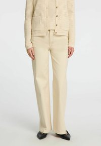 Béžové široké kalhoty vyrobené z bavlněné směsi, s měkkou texturou a vysokým pasem, doplněné odpovídajícím pleteným kardiganem.