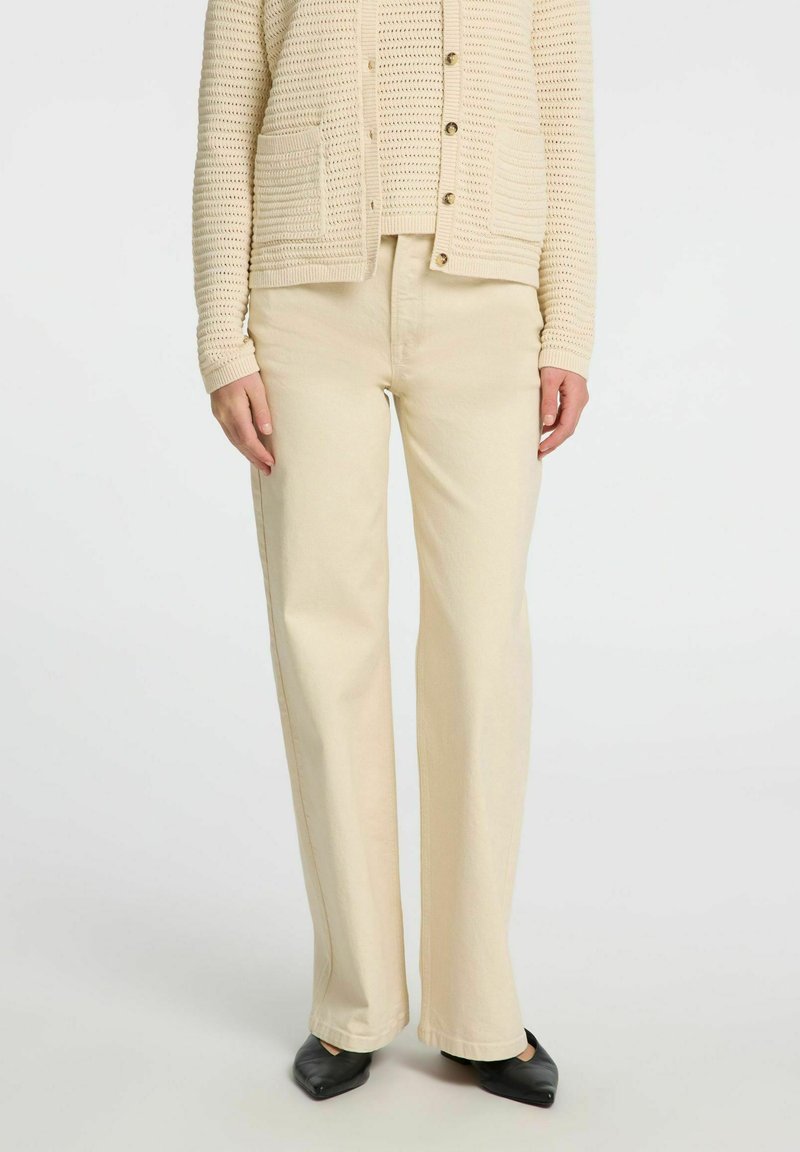 Béžové široké kalhoty vyrobené z bavlněné směsi, s měkkou texturou a vysokým pasem, doplněné odpovídajícím pleteným kardiganem.