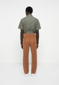 Brown corduroy pants with a relaxed fit, elastic waistband, and back pockets. Paired with a green patterned short-sleeve shirt.