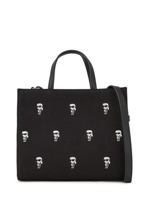 Bolso negro con asas cortas, una correa larga y un patrón de pequeñas figuras de dibujos animados blancas con gafas de sol distribuidas uniformemente en la parte delantera.