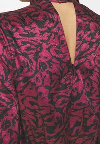 Tissu à motifs fuchsia et noir avec un design léopard, présentant un col montant, un dos ouvert et une texture lisse.