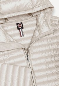 Svetlo bež prešit jakna s kapuco, sprednja zadrga in etiketo Colmar Originals na notranjem ovratniku.