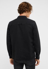 Czarna koszula z denimu, z długimi rękawami, kołnierzykiem i zapinanymi mankietami. Minimalistyczny design zawiera przeszycia i zaokrąglony dół.