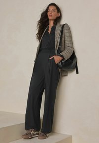 Gray plaid blazer over a black button-up shirt, paired with wide-leg black trousers and brown sneakers. A black bag is worn over the shoulder.