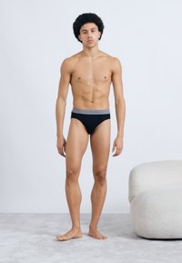 Fekete úszónadrág szürke elasztikus derékpánttal, férfi modell által bemutatva. A nadrág sima textúrájú és testhezálló kialakítású.