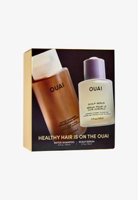 Set regalo per la cura dei capelli OUAI in una scatola dorata, con una bottiglia di shampoo detox marrone e una bottiglia trasparente di siero per il cuoio capelluto con tappo viola.