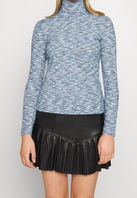 Maglione a collo alto a maniche lunghe blu a fantasia realizzato in tessuto a costine, abbinato a una gonna nera plissettata in ecopelle con orlo svasato.
