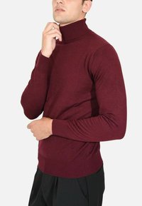 Maglione a collo alto borgogna realizzato in tessuto morbido, design aderente, con maniche lunghe e colletto e polsini a costine, abbinato a pantaloni neri.