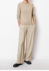 Beige Strickpullover mit langen Ärmeln, kombiniert mit beigen weit geschnittenen Hosen. Schwarze Stiefel mit dicker Sohle vervollständigen das Outfit. Weiche Textur, lockere Passform.