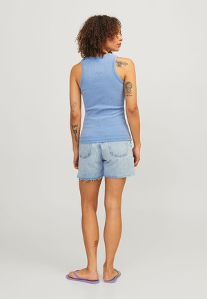 Blå ribbet tanktop med en tætsiddende pasform, parret med slidte lyse denimshorts; modellen står med ryggen til og har lilla flip-flops på.