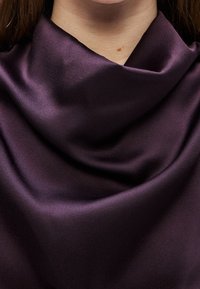 Gros plan sur le cou et les épaules d'une personne drapés dans un tissu satin lisse violet foncé formant de doux plis.