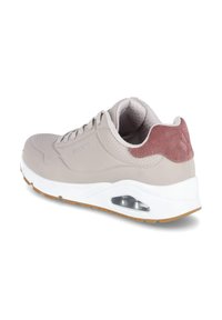 Zapatilla Skechers beige con suela blanca, suela de goma marrón, parte delantera con cordones, detalles perforados y acento en ante rosa en el talón.