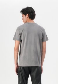 T-shirt de algodão cinza com um corte relaxado, mangas curtas, gola redonda e uma textura sutil. A vista traseira mostra um tecido liso com detalhes mínimos.