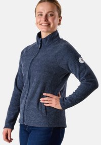 Giacca zip-up blu navale con un motivo testurizzato, colletto alto e design aderente. Presenta dettagli neri e un logo sulla manica sinistra.