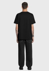 Czarna bawełniana koszulka z krótkim rękawem, okrągłym dekoltem. Nosi się z ciemnymi dżinsami o kontrastowym szwie i luźnym kroju.