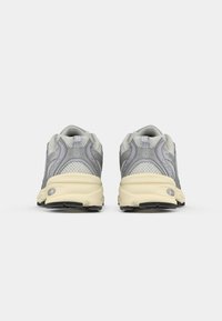 Une paire de baskets de sport grises et beiges vues de l'arrière, dotées d'un matériau en maille et synthétique avec une semelle rembourrée sur un fond blanc.