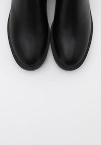 Botas de cuero negras hasta el tobillo con punteras redondeadas, textura suave y suela de goma baja. Sin embellishments ni patrones visibles.
