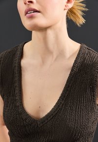 Braunes, strukturiertes Oberteil mit tiefem V-Ausschnitt, geprägt von einer gekräuselten Oberfläche und einer figurbetonten Silhouette. Der Hintergrund ist dunkel und unauffällig.