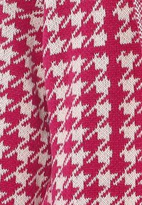Rózsaszín és fehér houndstooth mintás kötött anyag. Puha textúra, amely meghatározott formákat tartalmaz, erőteljes vizuális kontrasztot teremtve.
