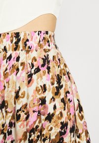 Gonna floreale con vita elastica, realizzata in tessuto leggero con un motivo astratto rosa, marrone e nero su uno sfondo crema.