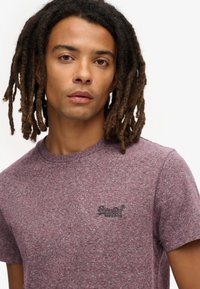 T-shirt met korte mouwen en ronde hals, gemaakt van een gestructureerde bordeauxrode stof met een subtiele heatherpatroon en een klein zwart logo op de linkerborst.