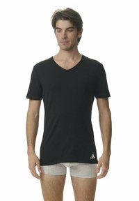 Svart V-ringad T-shirt i mjukt tyg med korta ärmar och en subtil logotyp på nedre vänstra sidan. Bärs med ljusgrå shorts.