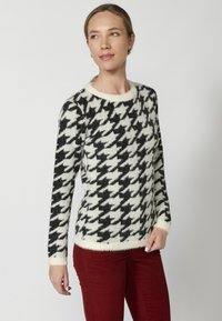 Pulover cu model houndstooth alb-negru din material pufoasă, cu guler rotund și mâneci lungi, asortat cu pantaloni burgundy.