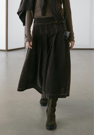 Brun højtaljet nederdel med plisseringer, lavet af blødt stof, kombineret med mørkebrune ankelstøvler og en tætsiddende langærmet top.