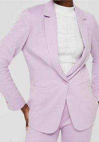Blazer violet clair en tissu lisse, avec un col cranté, une fermeture par un seul bouton et des poches latérales, associé à un haut blanc.