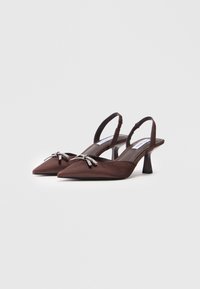 Zapatos de tacón slingback de satén marrón con punta afilada, un tacón bajo de bloque y detalles decorativos de moño con acabado en tono plateado.