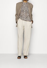 Blazer beige, blouse imprimé animal, pantalons crème. Sandales noires à bout ouvert. Lignes épurées, tissu léger et coupe décontractée.