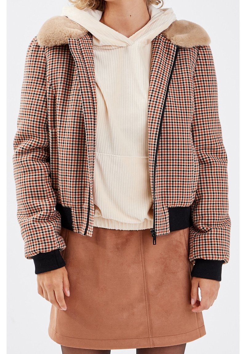 Röd och svart rutmönstrad bomberjacka med plyschkrage, svarta ribbade manschetter och dragkedjestängning, kombinerad med en krämvit hoodie och brun kjol.