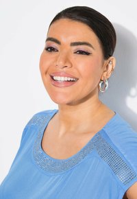 Ljusblå topp med rund halsringning prydd med silvernitar, korta ärmar och en mjuk textur i en avspänd passform.