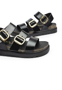 Sandalias de plataforma negras con tres correas anchas, hebillas doradas y una plantilla de corcho texturizada. Suela de goma con un patrón en zigzag.