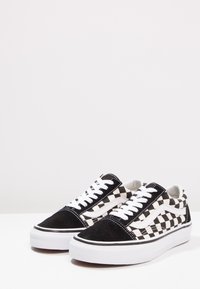 Sort og hvidt ternet ruskind og canvas sneakers med hvide snørebånd, polstret krave og gummiydersål. Flad design og lav profil.