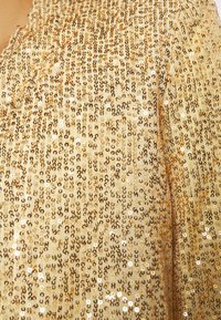Tessuto dorato con paillettes, caratterizzato da una texture scintillante e da un motivo geometrico di paillettes circolari in diverse tonalità di oro.
