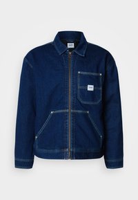 Donkerblauwe denimjack met een rits aan de voorkant en een borstzak. Heeft twee lagere zakken en witte stikselaccenten.