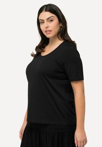 T-shirt nera a maniche corte con scollatura rotonda, realizzata in morbido cotone; texture liscia e vestibilità rilassata. Indossata sopra una gonna nera.