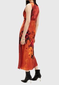 Oranges Blumenkleid mit einem taillierten Oberteil und schwingendem Rock, ausgestattet mit lebhaften roten und gelben Mustern; kombiniert mit schwarzen Knöchelstiefeln.
