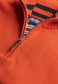 Oranger Zip-Up-Pullover mit strukturiertem Strick, ausgestattet mit einem gestreiften Kragen in Marineblau und Orange, sowie einem silbernen Reißverschluss mit einem Leder-Ziehfänger.