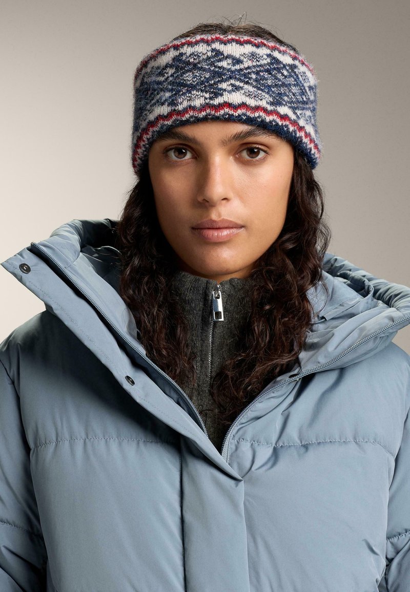 Knitted headband with a blue, white, and red pattern. Features a soft texture. Worn with a light blue puffer jacket and gray zip-up sweater.