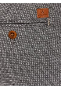 Tessuto grigio scuro con un motivo testurizzato, che presenta un bottone e un'etichetta in pelle marrone goffrata con la scritta "JACK & JONES."