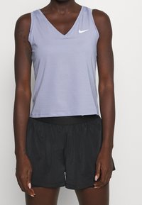 Top morado acanalado sin mangas con escote en V y logo blanco de Nike; combinado con pantalones cortos negros y ligeros con cintura elástica.