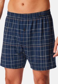 Boxer shorts a quadri blu navy con cintura elastica, dotati di un dettaglio con bottone e un motivo a griglia bianca e marrone chiaro a contrasto.