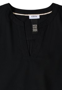 Chemise noire à col en V avec un col cousu, comportant des étiquettes de marque portant les inscriptions "CECIL" et "sea SIDE" avec des icônes de vagues à l'intérieur de l'encolure.