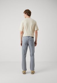 Jeans rectos de hombre en azul claro con un acabado desgastado y bolsillos delanteros y traseros, combinados con una camiseta de manga corta beige.