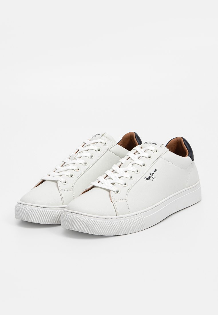 Baskets blanches en cuir avec une texture lisse, bout rond, lacets ton sur ton et un accent en cuir marron au talon. Elles possèdent une semelle en caoutchouc blanc texturé.