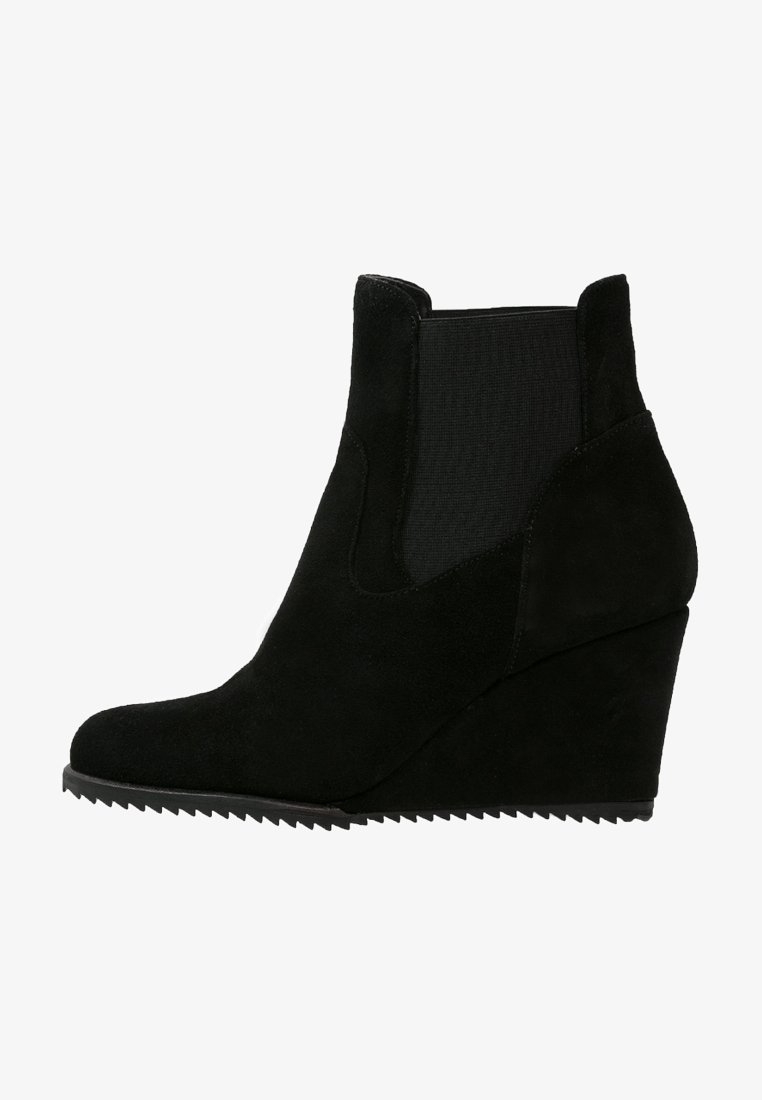 Botte compensée en daim noir avec panneau latéral élastique et semelle crantée, conçue pour une tenue décontractée ou habillée.