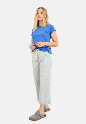 Blaues kurzärmeliges T-Shirt kombiniert mit hellblauen gemusterten Hosen mit Rüschensaum, ergänzt durch graue Clogs mit braunem Akzent.